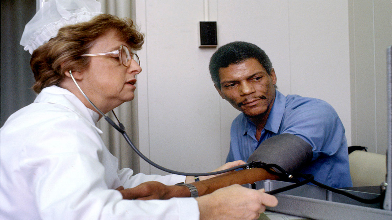  A doctor is taking the blood pressure of a patient while looking at a chart on the wall behind him.